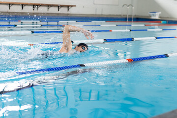 Caucasian young male swimmer wearing goggles, training indoors in swimming pool, copy space