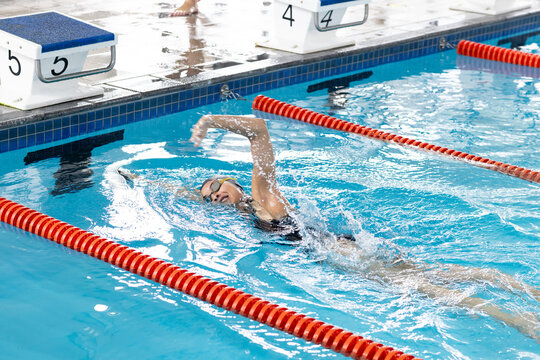 A biracial young female swimmer wearing goggles, training in indoor swimming pool