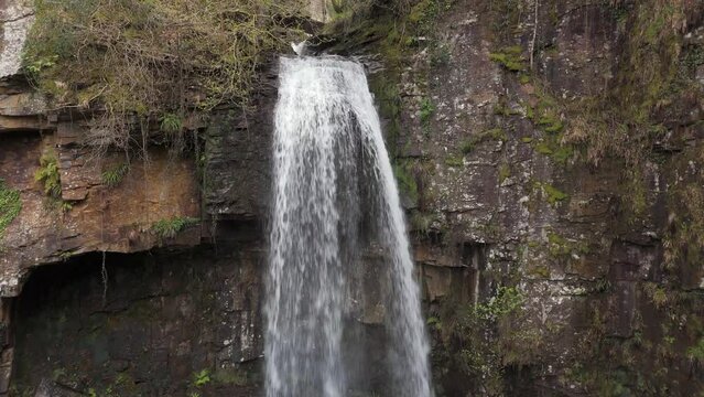 An aerial view of Melinclourt Waterfall on an overcast day, Neath Port Talbot, South Wales. Flying down the face of the fall from top to bottom