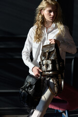 Naklejka premium beautiful curly blond hair woman posing with a two leather backpacks