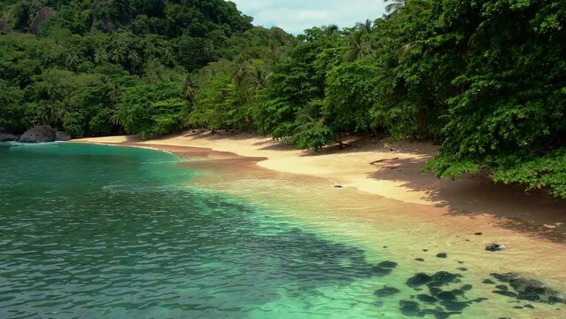 Drone flyover empty beach with turquoise colored water in lush forest of Principe Island