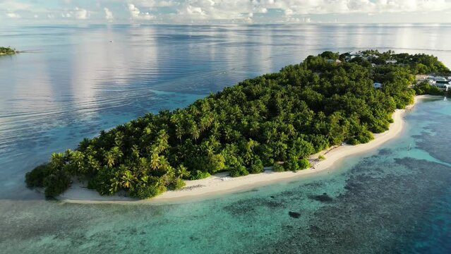 Aerial drone video slowly flying around the local island of Thinadhoo at sunrise in the Maldives.