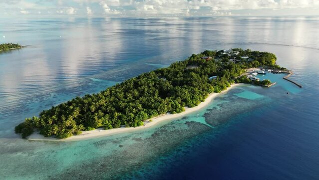 Drone footage slowly panning around the local island of Thinadhoo early in the morning, with clear blue waters in the Maldives.