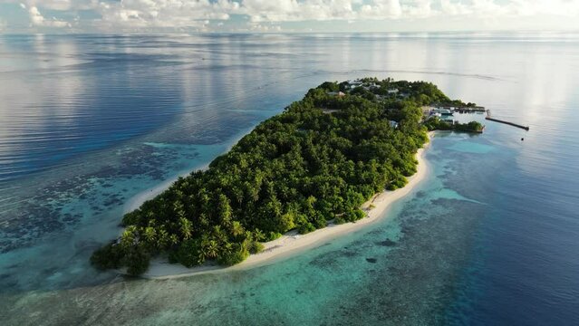 Aerial drone video panning around the small local island of Thinadhoo at sunrise in the Maldives.