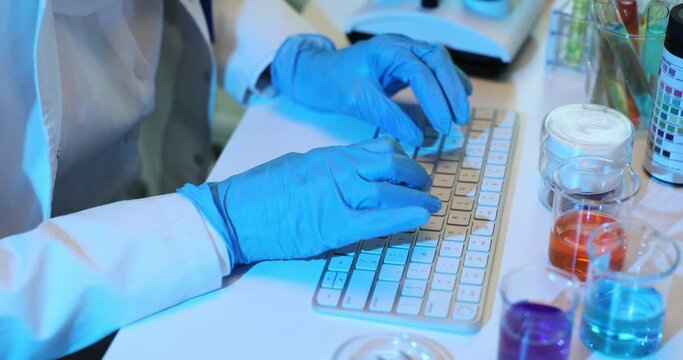 Scientist in blue gloves works at computer in laboratory