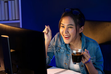 Smiling young beautiful Asian creative officer looking on pc in sales target online while holding...