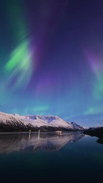 Aurora and snow covered mountains reflecting in a beautiful fjord in April in northern Norway.