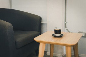A wooden table with a black coffee cup and a spoon