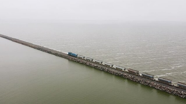 Long industrial freight train on straight track by sea in Argentina, aerial pan