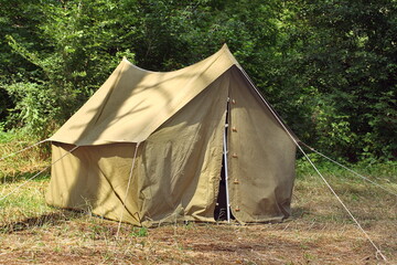  An old khaki tent stands on dry grass.