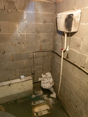 Dirty toilet room with pile of used toilet paper in the corner, uncoated concrete flooring and...