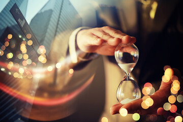 Close up of a businessman holding hourglass. Office. Morning cityscape. Concept of time management. Mock up. Toned image. Double exposure