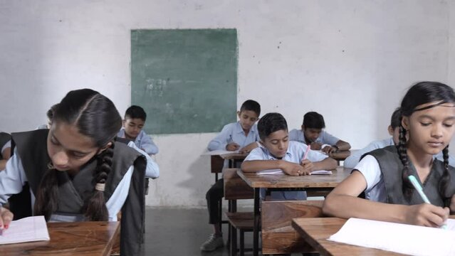 Rural Indian school students study in classroom. Elementary boys and girls writing doing classwork, test or exams, Education in india concept