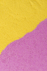 Close-up of a textured sand surface with a bright yellow top and a vibrant purple bottom. The granular texture and vivid colors provide strong contrast