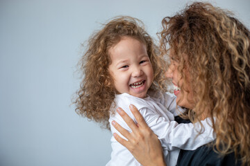 Curly mother and daughter play and laugh on a white background