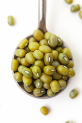Dry, green mung beans in iron spoon on white background. Close-up