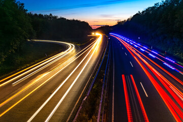 Yellow and red light traces of cars in motion. Blue flashlights of passing ambulance, fire fighter emergency vehicle. German motorway A46 after sunset at junction „Iserlohn-Zentrum“ in Sauerland.  - obrazy, fototapety, plakaty