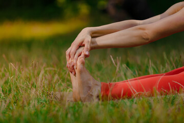 Closeup of young woman flexing feet while stretching on yoga mat outdoor. Solo stretch: Young woman finds solace stretching legs in lush park.