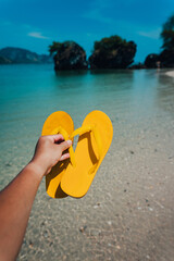 Yellow sandals in hand at the beach into the sea