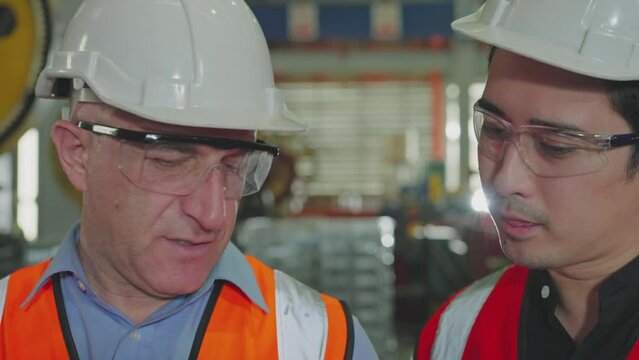 Two maintenance engineers in hard hats are intently reviewing data on a digital tablet at an industrial plant, Slow Motion