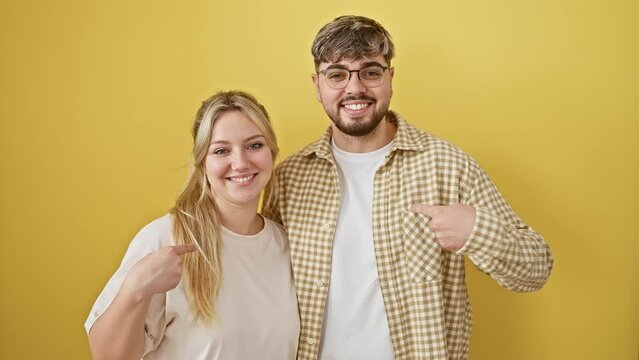 Beautiful couple ecstatically pointing together, joy marked on their smiling faces against vibrant yellow isolated background