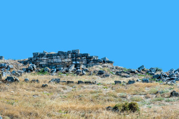 Ruined stone structures scattered in a field under a clear blue sky at ancient site of Hierapolis in Pamukkale, Turkiye