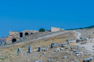 Stone arches and road amidst ruins under a bright blue sky at ancient site of Hierapolis in Pamukkale, Turkiye