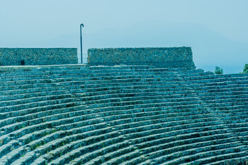 Cyan-toned ancient stone amphitheater with rows of seats depicting historical open-air venue at...