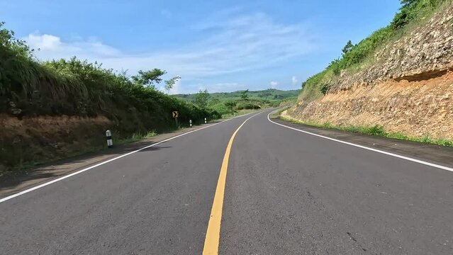 A beautiful curved road with hills on the side and blue sky in the background. in Blitar, East Java, Indonesia. JLS stand for Jalur Lintas Selatan (South Cross Lane) 