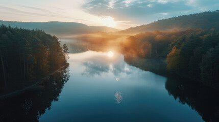 Aerial view of sunrise over a calm lake surrounded by forest, peaceful morning light on the water