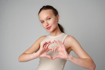 Young woman gesturing heart shape with hands on gray background