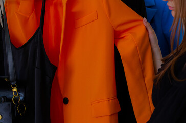Women hands touching wardrobe rack with stylish clothes indoors. Orange jacket, black dress and bag...
