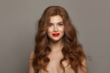 Young fashionable redhead woman with long wavy hair and make-up. Studio headshot portrait of fashion model lady with red colorful shine lipstick. Haircare, skin care and coloration concept - obrazy, fototapety, plakaty
