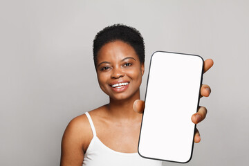 Smart healthy woman holding smartphone with white empty blank screen display on gray studio wall background. Happy model with phone