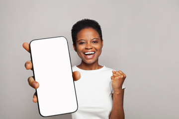 Successful woman showing smartphone with empty blank screen display. Model in white t-shirt with phone on gray studio wall background