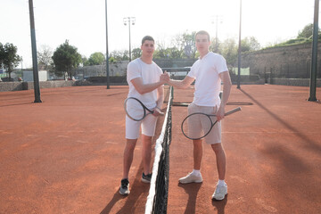 Two young male tennis players are portrayed on a court by the net