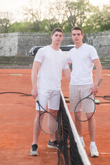Two young male tennis players are portrayed on a court by the net
