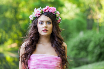 Portrait of healthy woman with makeup and long wavy dark brown hairstyle with flowers on head in spring park outdoor - 793649859