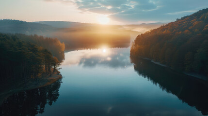 Aerial view of sunrise over a calm lake surrounded by forest, peaceful morning light on the water