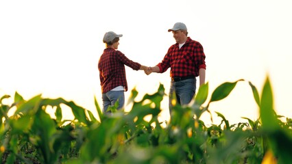 Two farmer agronomist colleagues shaking hand collaboration at corn field with sky. Man and woman...