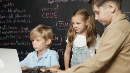 Closeup of boy using laptop programing engineering code and writing program while group of smart...