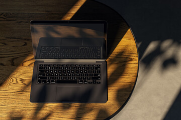 Top view of modern designer desktop with laptop on wooden desk, sunlight and shadows. 3D Rendering.