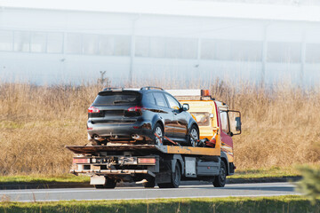 Roadside assistance. Tow truck transporting a broken car on a highway. Flatbed towing truck with a...