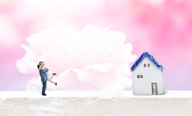 Miniature couple with vintage house model over blurred rose flower background, Love and romance concept, valentine background idea