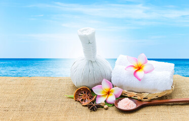 Herbs massage ball with dry herbs and pink salt in wooden spoon over blurred tropical beach background, Spa and wellness concept