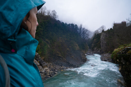 Hooded woman observing a river on a rainy day.