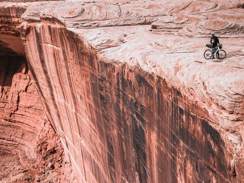 cyclist stands at edge of tall sandstone cliff, Canyonlands Park, Uta