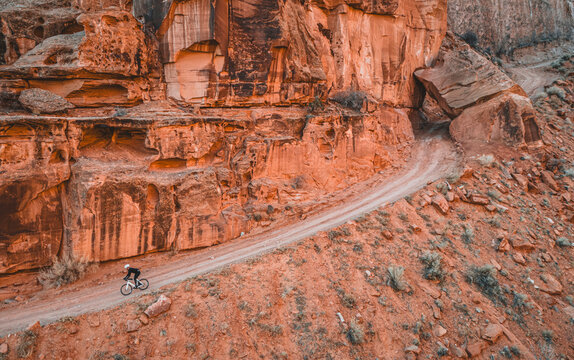 Man rides bike down narrow dirt road on cliff face, Moab, Utah