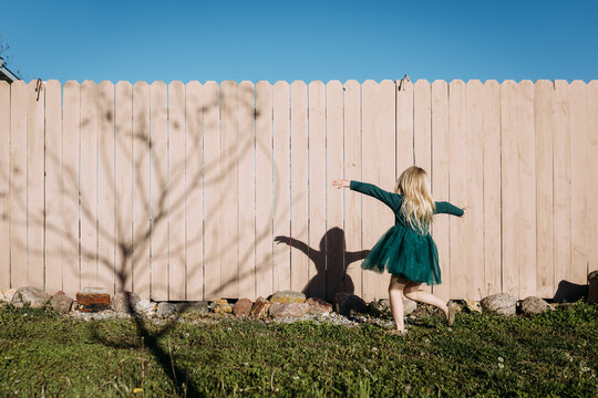 Girl dancing in yard casting shadow on pink fence