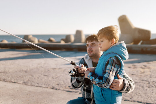 A young father with a small toddler son outdoors fishing by a sea